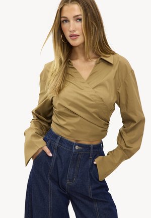 Chemise marron à manches longues enroulée avec un col et des manches évasées, associée à un pantalon en denim bleu foncé taille haute avec poches avant.