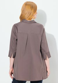 Tunic marrone leggero con maniche tre quarti, colletto e un dettaglio plissettato sul retro. Gli spacchi laterali all'orlo aumentano il comfort.