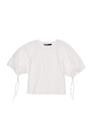 White cropped top with soft, textured fabric, puffed sleeves, and adjustable drawstrings at the cuffs. Round neckline and minimalist design.