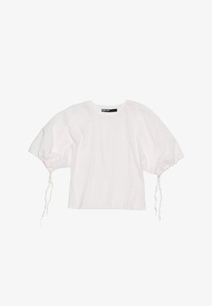 Crop top blanc en tissu doux et texturé, avec des manches bouffantes et des cordons de serrage ajustables aux poignets. Encolure ronde et design minimaliste.