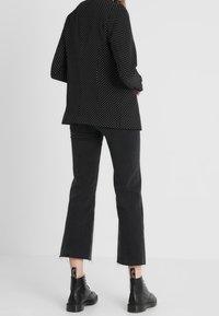 Czarny żakiet w kropki o luźnym kroju, zestawiony z krótkimi czarnymi dżinsami z postrzępionymi nogawkami oraz czarnymi botkami za kostkę.