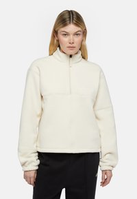 Pullover in pile crema con colletto alto e zip a metà. Presenta una superficie testurizzata e polsini elasticizzati, completato da un branding discreto.