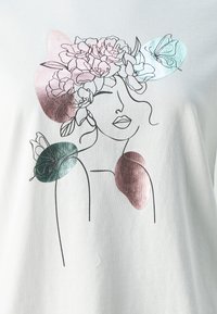 White t-shirt featuring a line-drawn face adorned with pink flowers and butterflies, with metallic accents in green and rose gold.