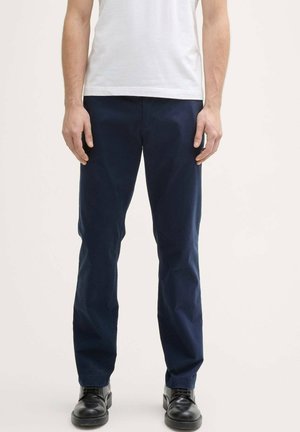 Pantalons en coton bleu marine avec une coupe droite, présentant une texture lisse et des poches avant, accompagnés de chaussures noires.