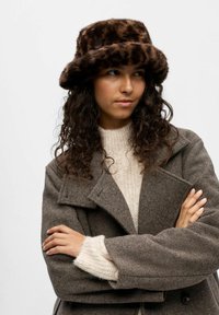 Brun leopardmönstrad faux fur bucket hat. Mjuk textur med bred brätte. Bärs med en ljus creamstickad tröja och en brun rock.