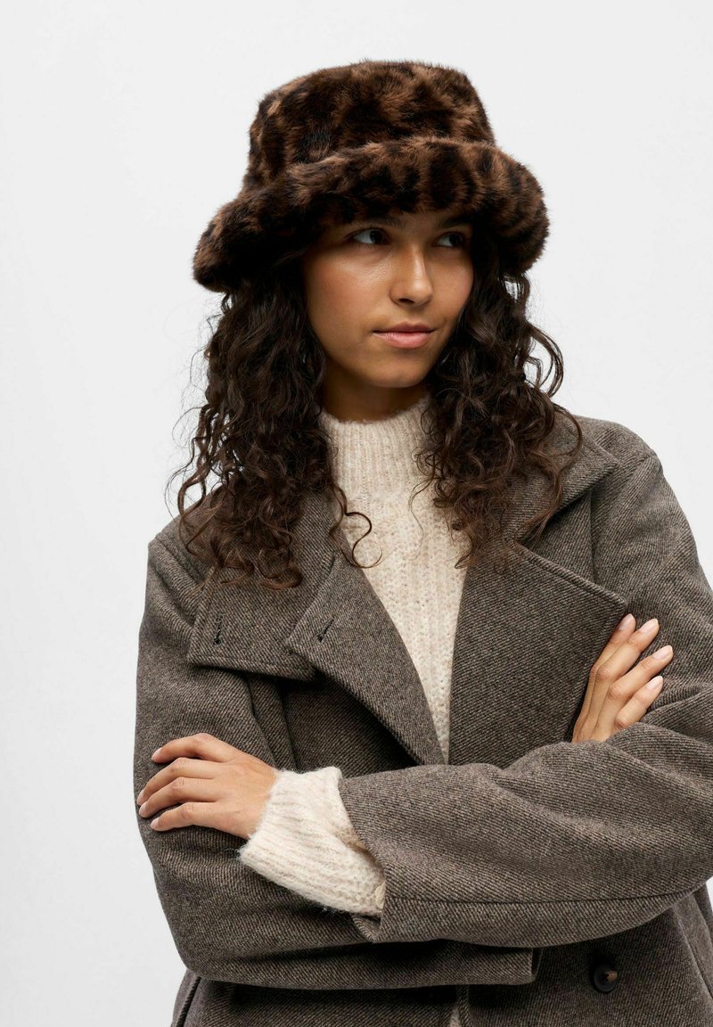 Brun leopardmönstrad faux fur bucket hat. Mjuk textur med bred brätte. Bärs med en ljus creamstickad tröja och en brun rock.