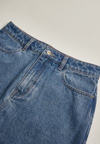 Närbild av blå denimjeansmidja med knapp, bältesöglor och framfickor på en neutral bakgrund.