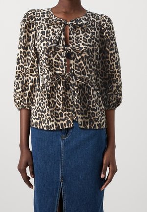 Kvinde iført en bluse med leopardprint, pufærmer og frontsløjfer, kombineret med et blåt denimskørt med frontslids.