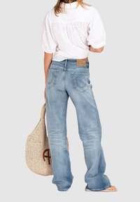 Jeans azzurri chiari a gamba larga con tasche posteriori e una patch in pelle. Abbinati a una camicia bianca con maniche a sbuffo e a una borsa a tracolla intrecciata.