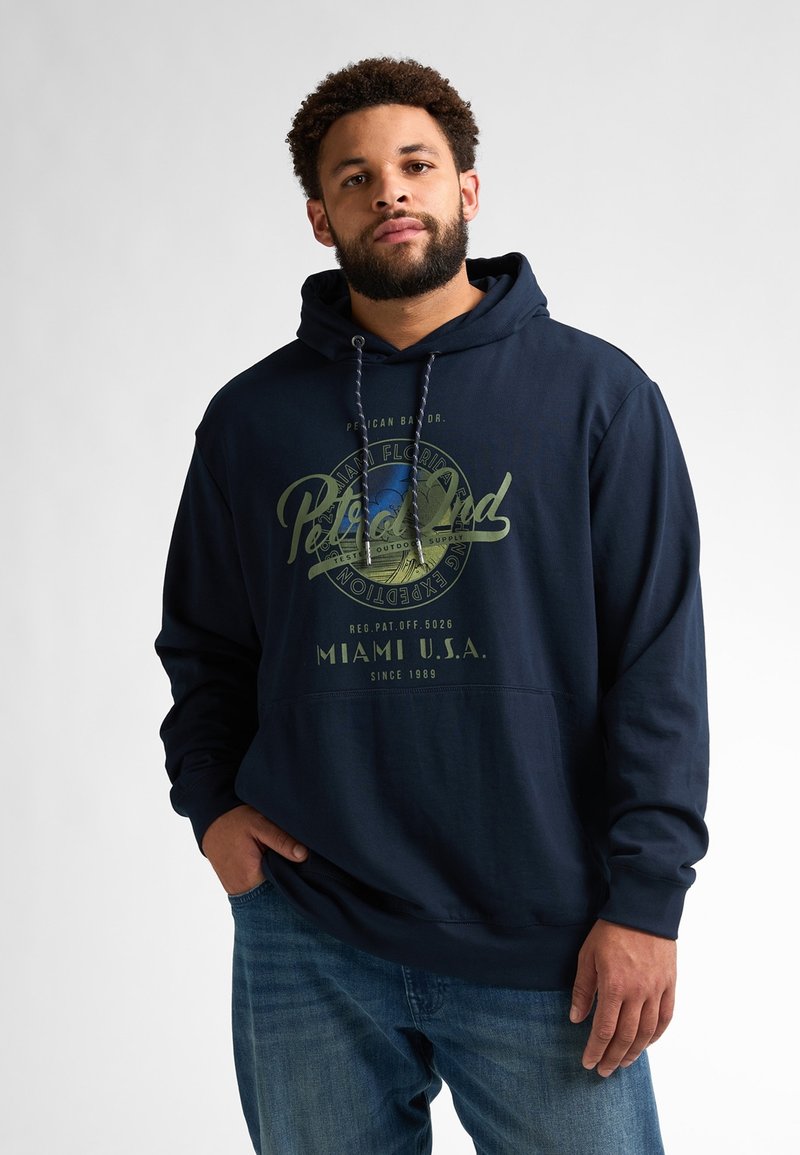 Námornícky modrá mikina s kapucí vyrobená z bavlny, na přední straně má velký potisk loga v zelené a bílé barvě. Detail klokání kapsy.