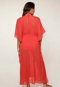 Cubierta roja y transparente con un patrón geométrico. Tiene un cuello halter y una cintura elástica, fluyendo hasta una longitud maxi.