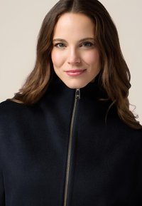 Chaqueta de mezcla de lana azul marino con cuello alto y detalle de cremallera dorada, que presenta una textura suave y un diseño limpio.