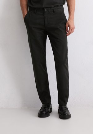 Zwarte katoenen broek met een recht model, voorzien van een knoopsluiting en zijzakken, gecombineerd met zwarte schoenen.