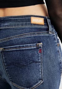 Donkerblauwe denim jeans met een leren label 'REPLAY', rode stikdetails op de zak en een klassieke vijf-pocketontwerp.