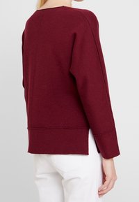 Burgunderfarvet sweater med lange ærmer, en rund halsudskæring og en afslappet pasform. Fremstillet af blødt materiale, med slidser i kanten for ekstra bevægelse.
