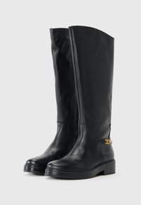 Bottes noires en cuir jusqu'au genou avec une texture lisse, bout arrondi et semelle épaisse. Comprend un accent doré au niveau de la cheville.