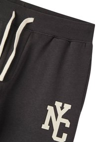 Pantaloni della tuta grigio carbone con una cintura elastica, coulisse bianche e una grafica "NYC" color crema sulla gamba sinistra.