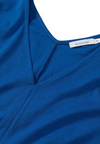 Blå V-ringad tröja med synliga stygn och en vit storleks- och varumärkesetikett på insidan av kragen som säger "hessnatur 36".