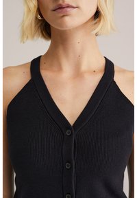 Czarna, bezrękawnikowa kamizelka z prążkowaną fakturą, głębokim dekoltem w serek i pięcioma guzikami z przodu. Materiał wydaje się miękki i dopasowany.
