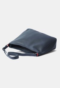 Marineblauwe leren schoudertas met een platte rechthoekige vorm, verstelbare schouderband en rode accenten in de hardware. Glad textuur, minimalistisch design.