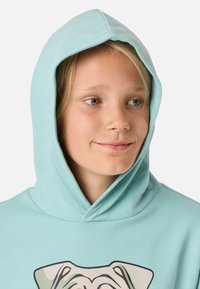 Felpa blu chiaro realizzata in morbido tessuto con cappuccio regolabile, caratterizzata da una stampa grafica di un cane sul davanti.