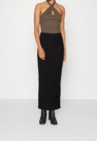 Haut marron à col licou avec un détail en forme de serrure, associé à une jupe noire côtelée longue jusqu'au sol. Le mannequin porte des bottines noires.