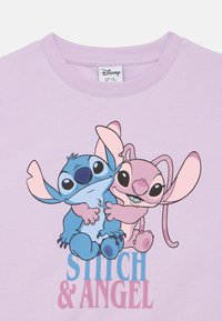 Light purple T-shirt featuring cartoon characters Stitch and Angel in vibrant blue and pink, with text "STITCH & ANGEL" in bold colors.