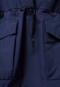 Navyblauwe jas met een soepele textuur, met een taille die is verstrakt, twee voorzakken en een verstelbaar trekkoord bij de halslijn.