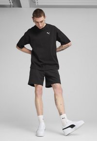 T-shirt en coton noir à manches courtes avec un petit logo blanc, assorti à un short noir. Baskets blanches avec des accents noirs et chaussettes à motifs.