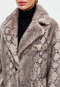 Műszőr kabát bézs és barna kígyóbőr mintával, kivágott gallérral és egy gombos záródással, valamint egy pattintós zsebbekkel.