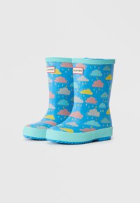Des bottes de pluie en caoutchouc bleues présentent un motif de nuages et de gouttes de pluie en rose, jaune et bleu clair. Semelle et bordure turquoise texturés.