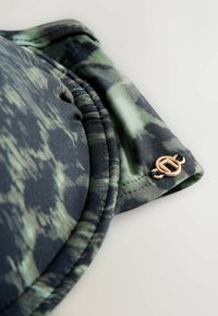 Top de bikini moale, cu imprimeu de camuflaj negru și verde. Are un accent metalic de culoare aurie și margini cusute pentru o fixare sigură.