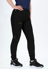 Black outdoor pants with a fitted design, featuring zippers and a logo. Constructed from durable material with a smooth texture.