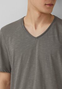 V-hals, korte mouwen t-shirt gemaakt van lichtgewicht, grijze stof met een subtiele textuur en stikdetails langs de halslijn.