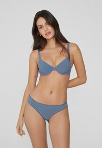 Blaue Unterwäsche mit einem BH mit Drahtunterstützung und verstellbaren Trägern, kombiniert mit passenden, niedrig geschnittenen Slips, beide aus einem glatten, einfarbigen Stoff.