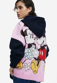 Kapuzensweatshirt mit pinkem Körper, der ein Design von Mickey und Minnie Mouse zeigt, dunkelblauen Ärmeln und strukturiertem Stoff mit floralem Akzent.