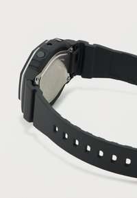 Μαύρο ψηφιακό ρολόι χειρός με λουράκι από καουτσούκ, μεταλλική πλάτη στερεωμένη με βίδες και ορατά κουμπιά ρύθμισης στο πλάι.