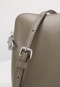 Borsa a mano grigia con texture, dotata di una tracolla regolabile coordinata, hardware in argento e etichetta. La superficie presenta una finitura sottile e dettagli di cucitura.