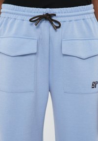 Svijetloplave joggerice od teksturiranog materijala, s dva prednja džepa, elastičnim pojasom i smeškim vezicom s detaljem logotipa.