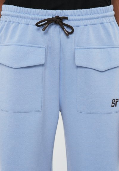 Calças de jogging azul claro feitas de um tecido texturizado, com dois bolsos frontais, uma cintura elástica e um cordão castanho com detalhe de logotipo.
