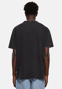 Schwarzes Baumwoll-T-Shirt mit lockerem Schnitt, kurzen Ärmeln und rundem Ausschnitt. Verfügt über sichtbare Nähte und eine leicht verblasste Textur.