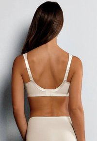 Beżowy biustonosz z gładkiego materiału, z regulowanymi ramiączkami i zapięciem na haftkę z tyłu. Posiada zaokrąglony, bezszwowy design.