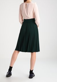 Vihreä poimutettu hame, jossa on leveä vyötärönauha, yhdistettynä vaaleanpunaiseen yläosaan, jossa on avainaukko-yksityiskohta. Mallilla on mustat sukat ja kengät.