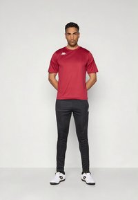 Rød trenings-T-skjorte med korte ermer, kombinert med svarte tettsittende bukser. Hvite treningssko med svarte detaljer fullfører antrekket.