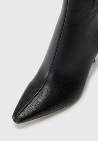 Bottine en cuir noir à bout pointu, avec une surface texturée et un design élégant. Des coutures discrètes soulignent la silhouette.