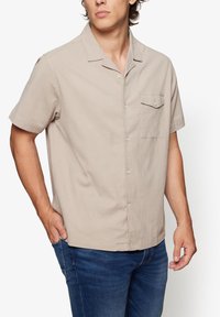 Short-sleeve beige shirt, textured fabric, buttoned with a chest pocket. Features a classic collar and a relaxed fit.