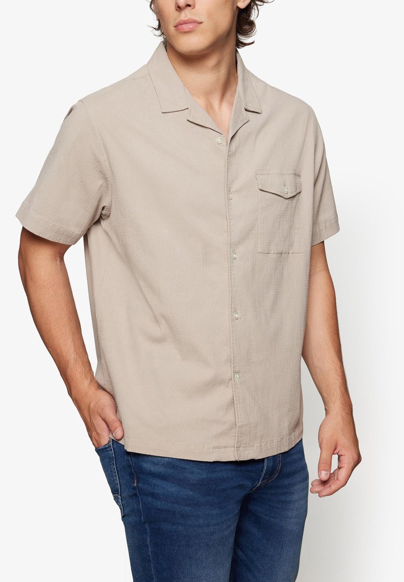 Short-sleeve beige shirt, textured fabric, buttoned with a chest pocket. Features a classic collar and a relaxed fit.