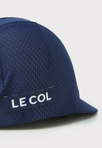 Marine sykkelhjelm laget av pustende mesh-materiale; har en buet brem og et hvitt "LE COL" logo-patch på siden.
