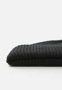 Złożona czarna dzianinowa czapka beanie o prążkowanej teksturze leży na białej powierzchni.
