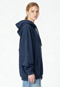 Felpa con cappuccio blu navy con tasca frontale, coulisse regolabili, polsini a coste e vestibilità oversize. Realizzata in morbido cotone.